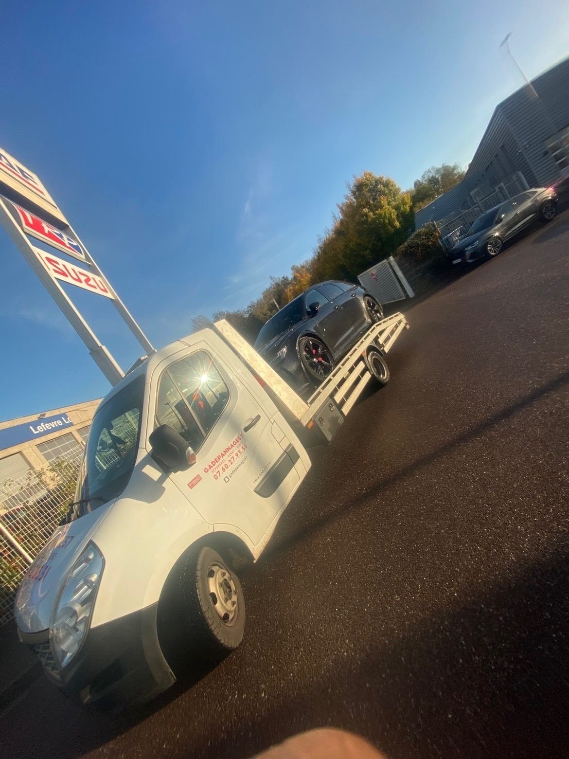 Dépanneuse plateau GA Dépannage chargée d’une voiture sombre sur un parking